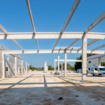 Ensemble de poutres béton préfabriquées formant la toiture d’un bâtiment, vues depuis l’entrée d'un site