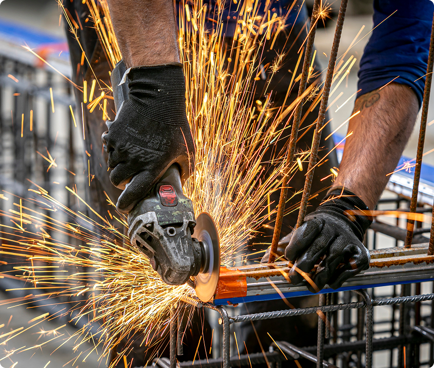 Gros plan sur un ouvrier CIR PREFA utilisant une meuleuse pour découper une armature métallique, illustrant la précision et la technicité du travail en usine